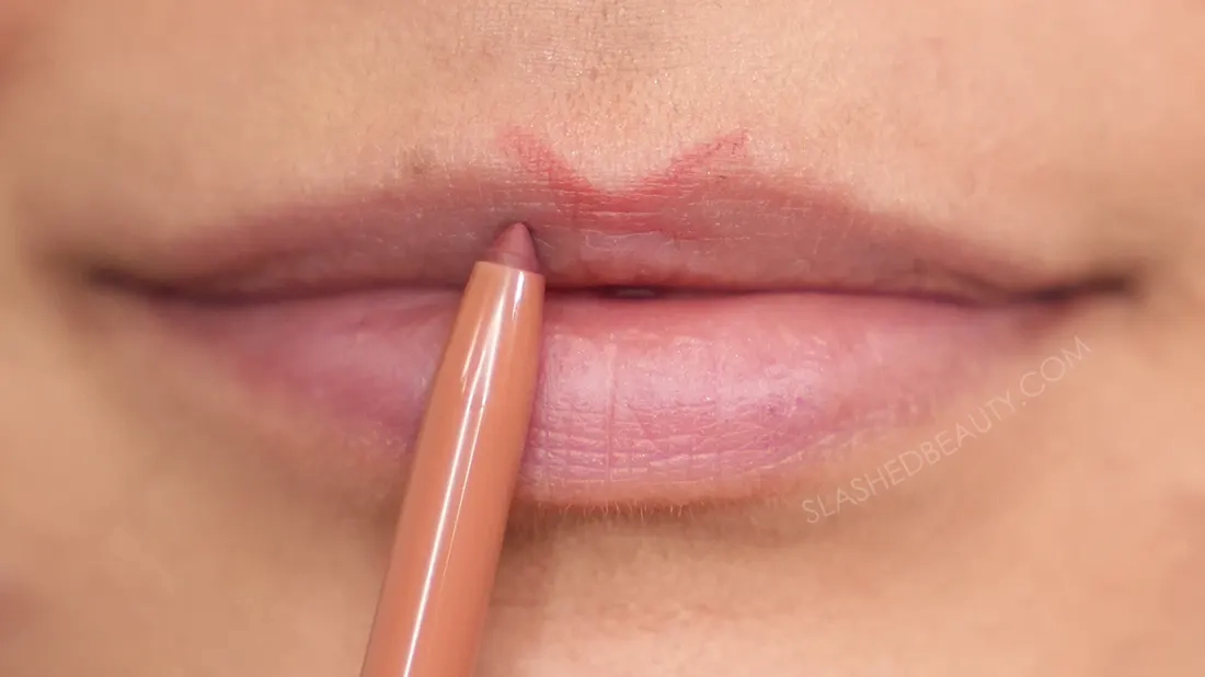 how-to-line-lips-bigger-1 | Slashed Beauty Close up of lip liner on lips drawn in an X shape on the cupid's bow. | How to Make Your Lips Look Bigger with Makeup | Slashed Beauty