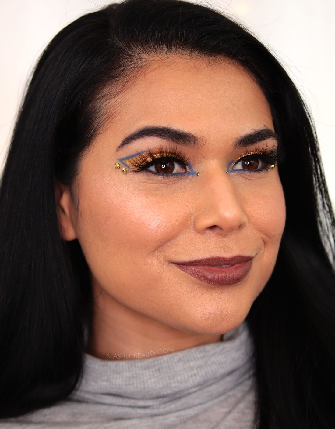 Miranda looking off camera wearing a bejeweled gold and blue eyeshadow look and brown lipstick. | 5 Daring 2022 Beauty Trends to Try This Year | Slashed Beauty