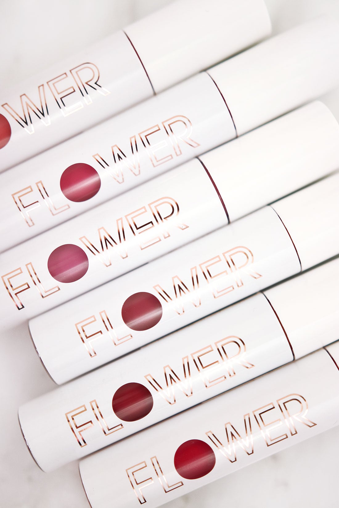 flower-beauty-bitten-stain-review | Slashed Beauty Tubes of Flower Beauty Bitten Lip Stains lying side by side on a marble surface | Flower Beauty Bitten Lip Stains Review & Swatches | Slashed Beauty