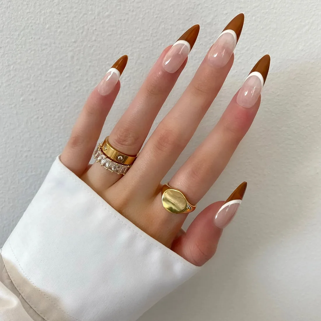 stilleto-brown-french-nails-fall | Slashed Beauty Close up of hand wearing stilleto nail press ons with a brown and white french tip design for fall | Trendy Fall Nail Designs You Can Buy as Press-Ons on Etsy | Slashed Beauty