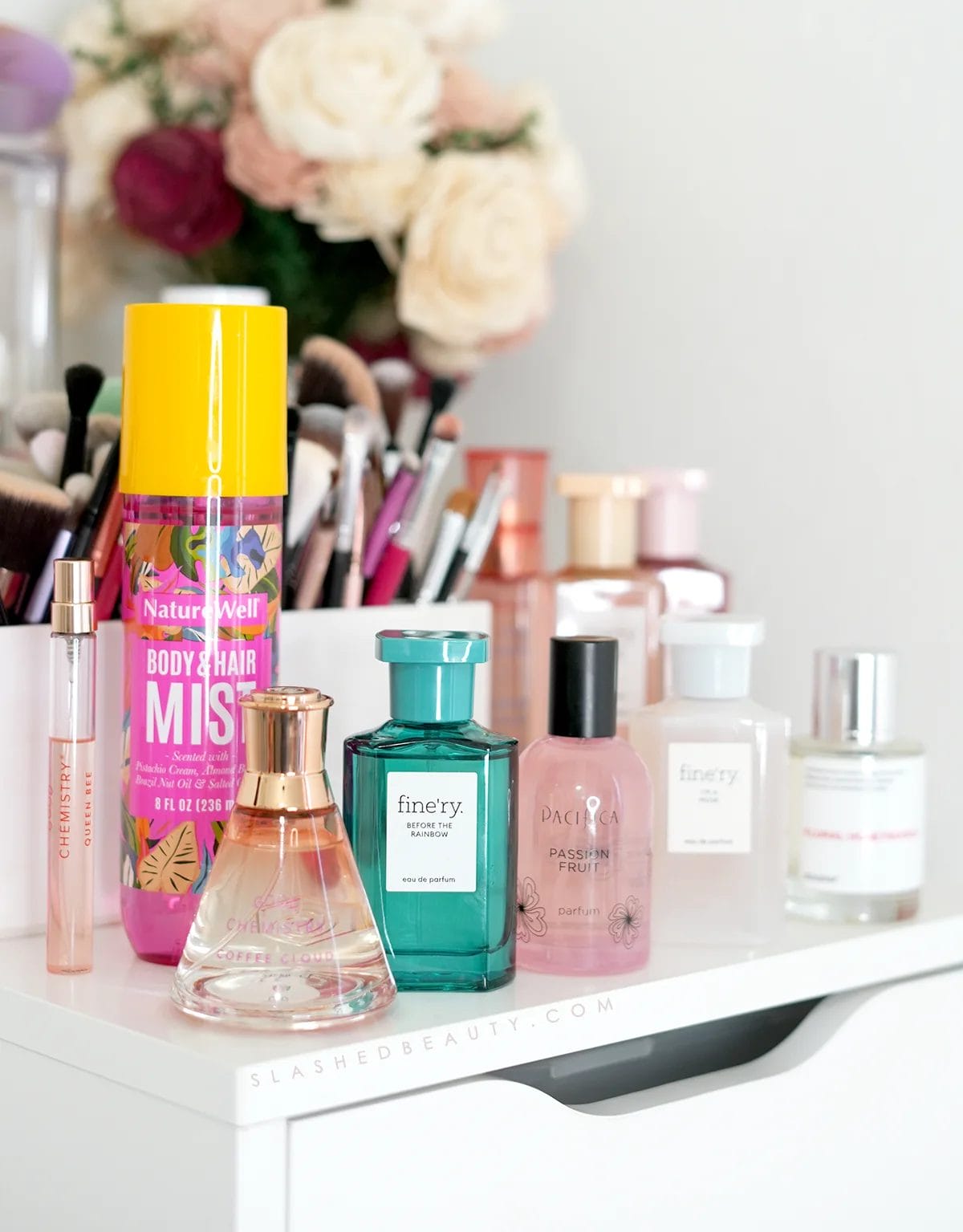 affordable-perfumes-fragrances | Slashed Beauty Various bottles of perfume sitting on top of a white dresser with makeup brushes in the background. | 7 Affordable Perfumes that Don't Smell Cheap | Slashed Beauty