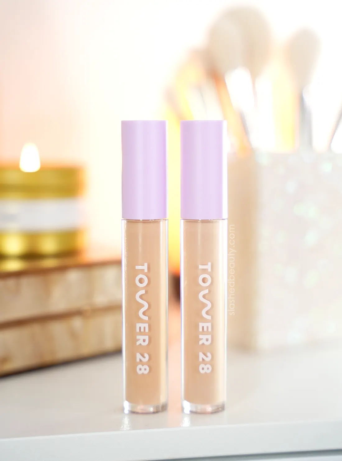 tower-28-SERUM-swipe-concealer-review-ie-lbc | Slashed Beauty Two tubes of Tower 28 Serum Concealer standing on a vanity with a candle and makeup brushes in the background. | Tower 28 Swipe All Over Serum Concealer Review on Dry Skin | Slashed Beauty